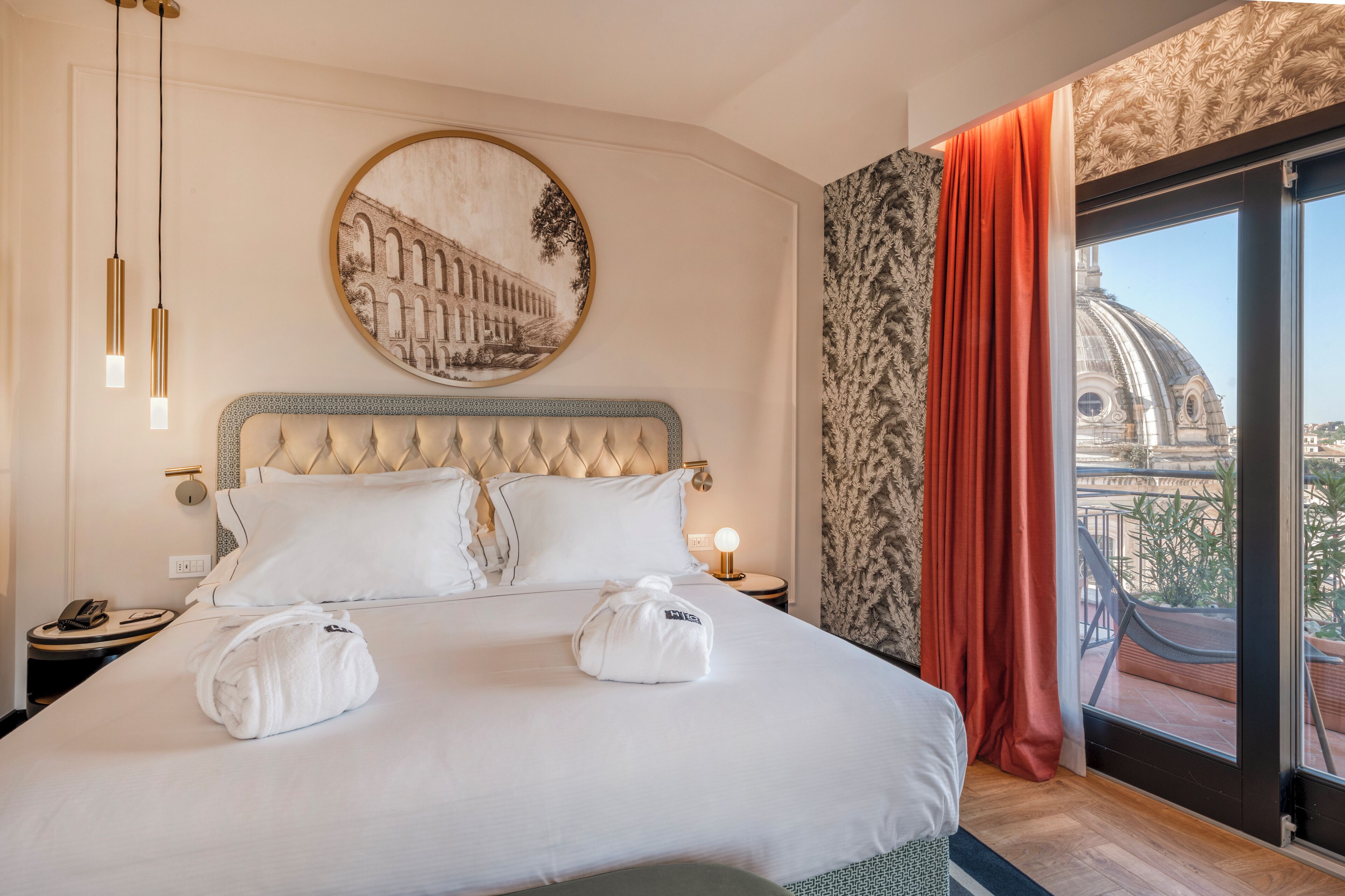 Une chambre d’hôtel avec un grand lit, un tableau rond accroché au mur, une table de chevet avec un téléphone et une vue sur un immeuble par la fenêtre.