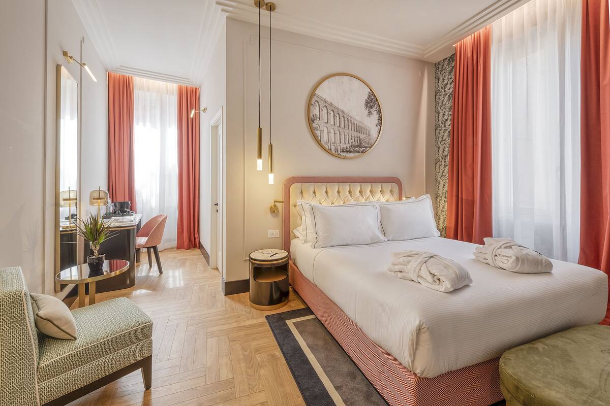A hotel room with a large bed, a desk with a chair, a small table with a plant, and a round wall decoration.