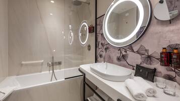 Un baño moderno con bañera, un espejo grande con luz y un tocador con lavabo y perchero para toallas.