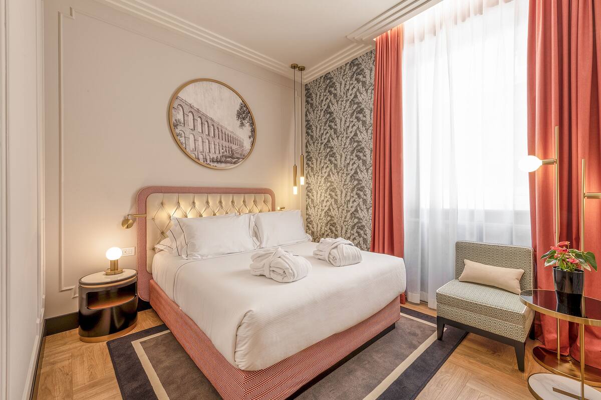A hotel room with a large bed, a bedside table with a lamp, a chair, and a wall-mounted picture.