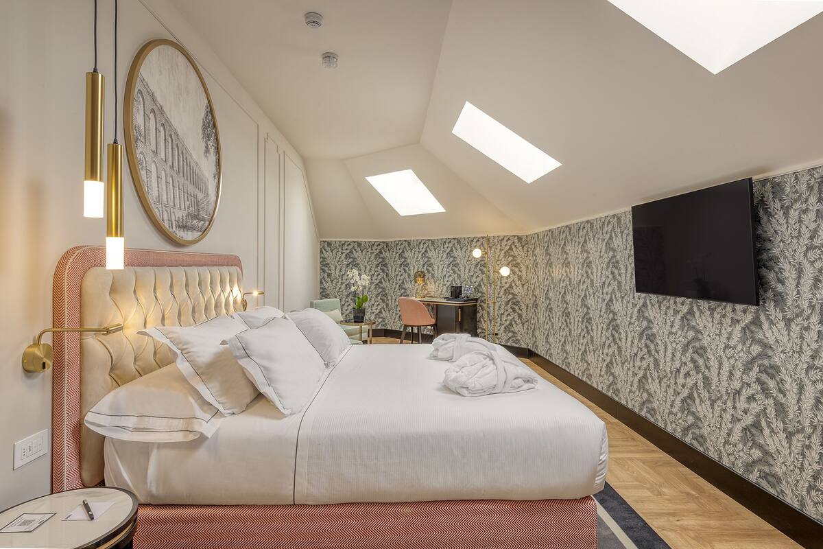 A modern hotel room with a large bed, a desk, and a TV on the wall.