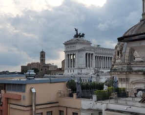 A classical building with columns and a statue on top, surrounded by other buildings. - H10 Palazzo Galla (Rome)