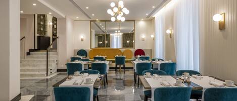 A hotel dining area with tables set for service, a staircase, and a large mirror reflecting the room.