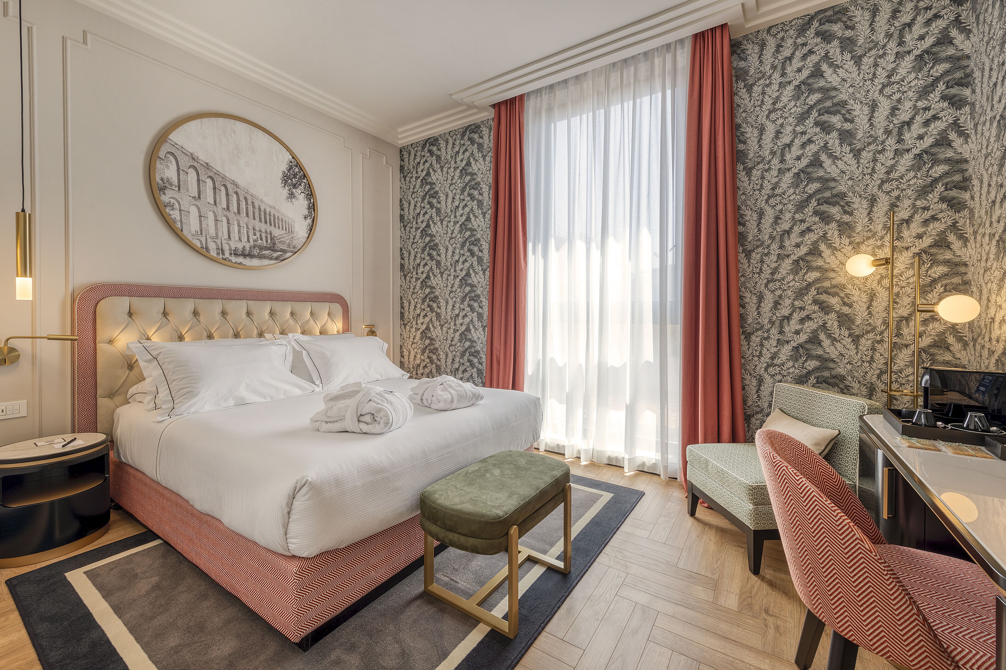 Habitación de hotel con una cama grande, zona de estar con una silla, escritorio y un ventanal con cortinas.