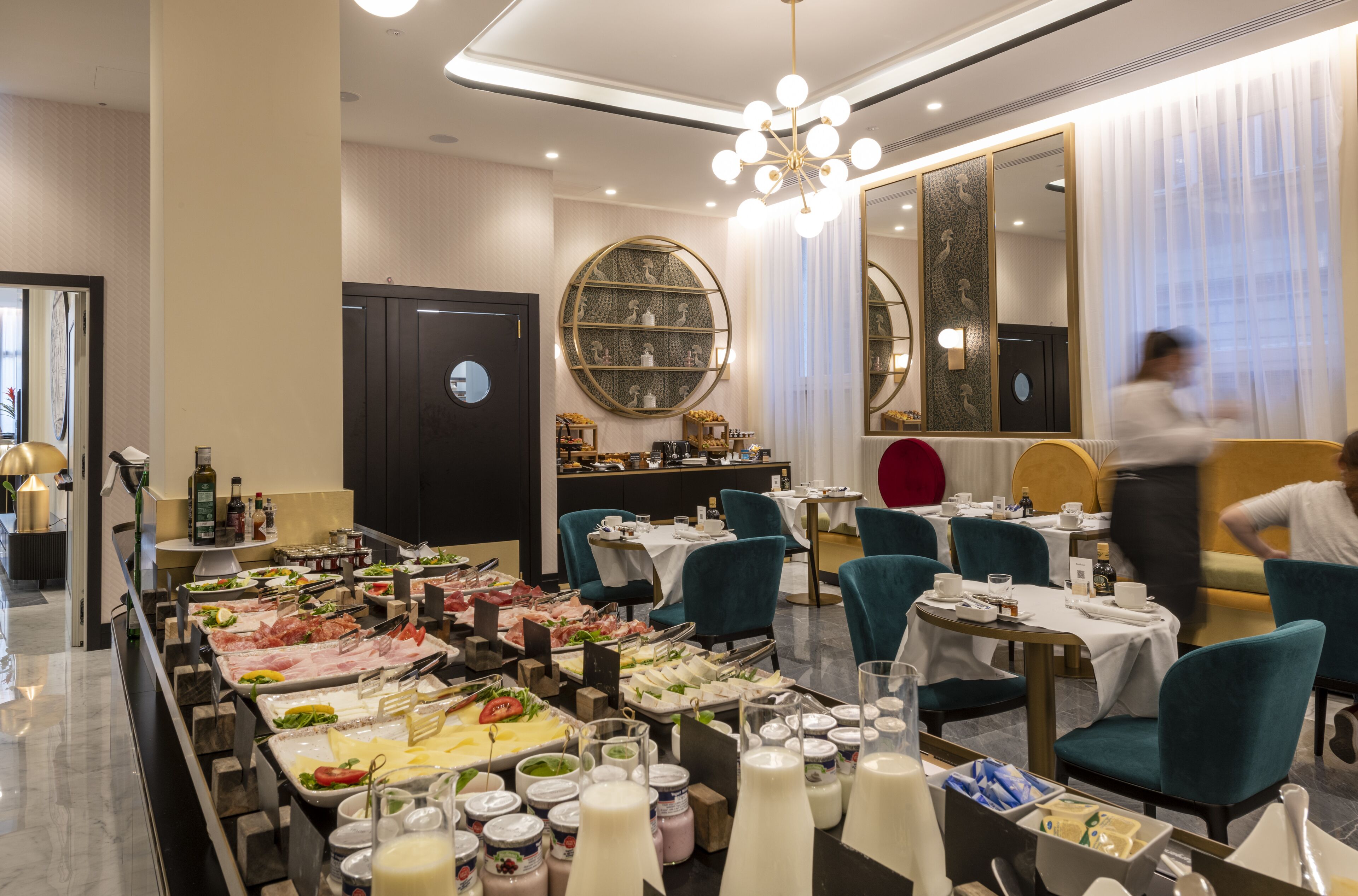 A buffet setup with various food items and beverages, a large mirror, and a chandelier.