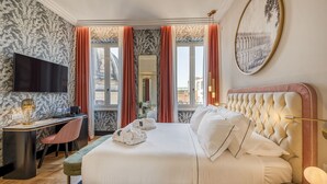 A hotel room with a large bed, a desk with a chair, a flat-screen TV, and a view of the city through large windows. - H10 Palazzo Galla (Rome)