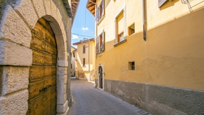 A narrow street with stone buildings, a wooden door, and a yellow wall. - Sergio Il Gufo Apartments (Toscolano Maderno)