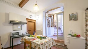 A kitchen with a dining table set for two, a microwave, a refrigerator, and a wooden door. - Sergio Il Gufo Apartments (Toscolano Maderno)