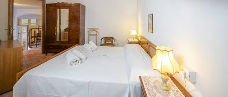 A hotel room with a bed, a wooden dresser, a mirror, a nightstand with a lamp, and a blue ceiling drape.