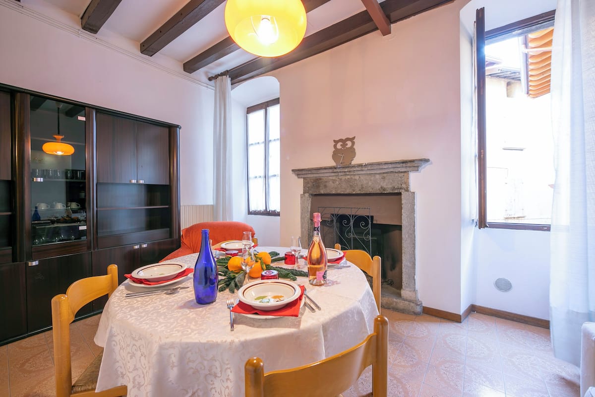 A dining room with a round table set for four, a fireplace, and a view of the outside through a window.