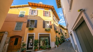 A narrow street with buildings featuring wooden shutters and balconies, a shop with mannequins, and a clear blue sky. - Sergio Il Gufo Apartments (Toscolano Maderno)