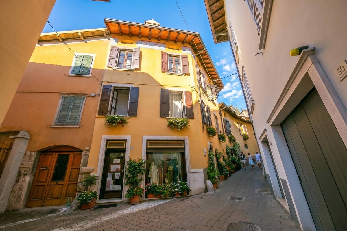 Eine enge Straße mit Gebäuden, die Holzhörner und Balkone haben, ein Geschäft mit Schaufensterpuppen und einem klaren, blauen Himmel.
