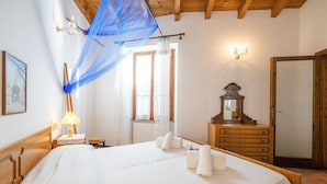 A hotel room with a bed, a wooden dresser, a mirror, a lamp, and a blue canopy. - Sergio Il Gufo Apartments (Toscolano Maderno)