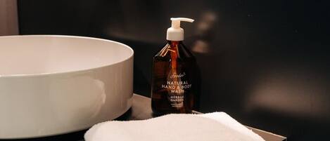 Un baño con un lavabo redondo, una botella de jabón natural para manos y cuerpo, y toallas dobladas.