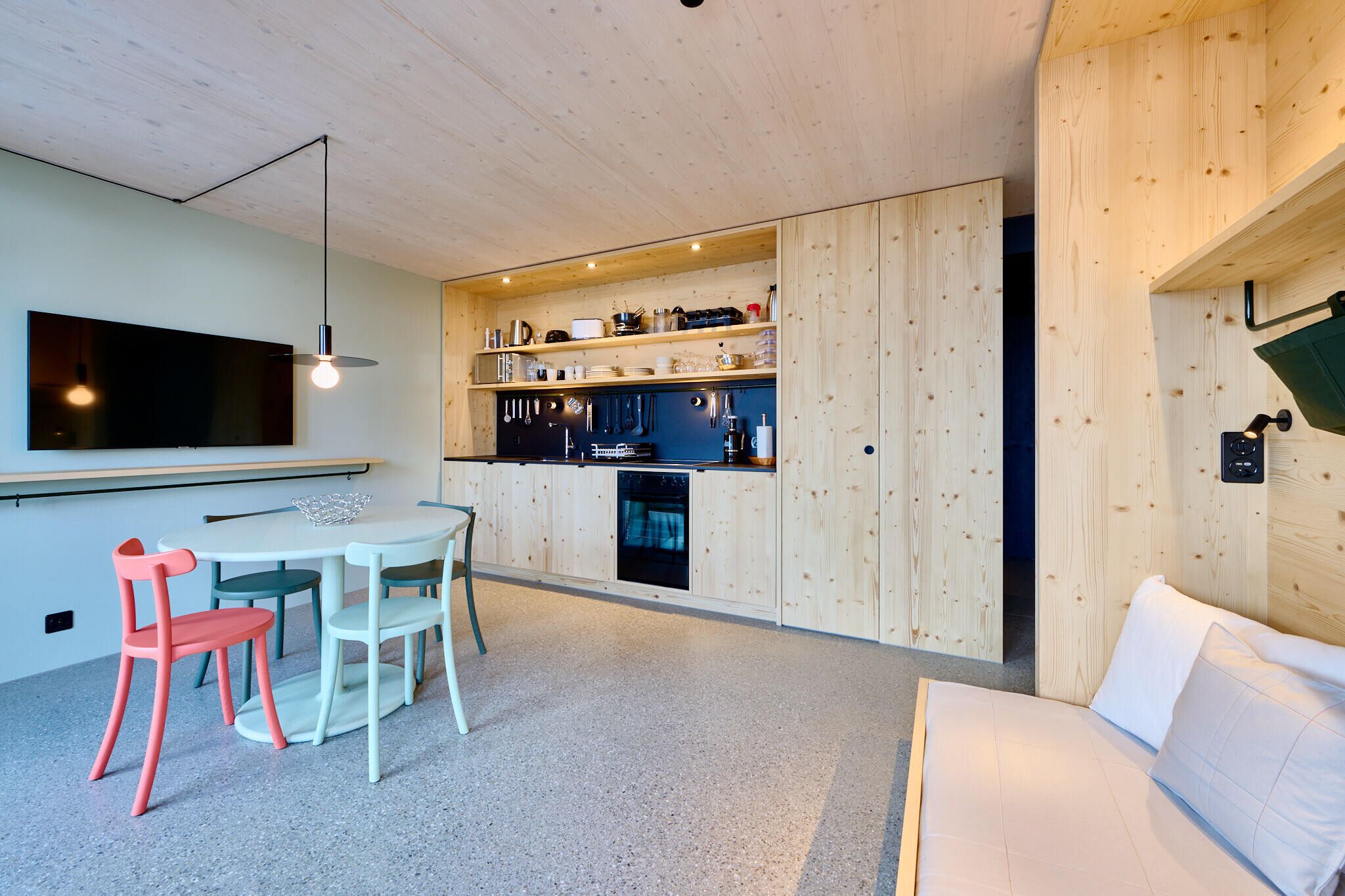 Una cocina moderna con armarios de madera, una zona de comedor con mesa y sillas, y un horno empotrado.