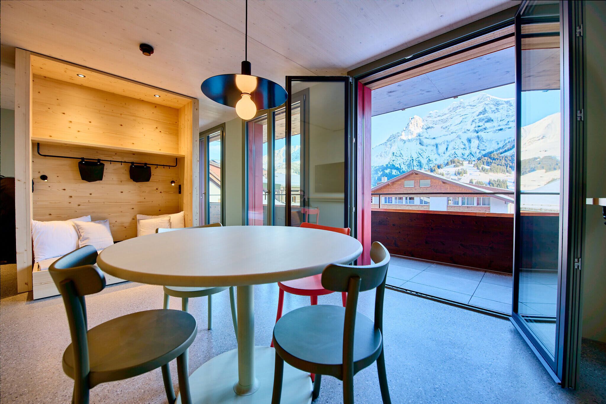 A modern room with a round table, two chairs, a hanging light fixture, and a view of a mountain landscape through large windows.