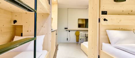 A compact hotel room with bunk beds, a small desk, and a mirror.