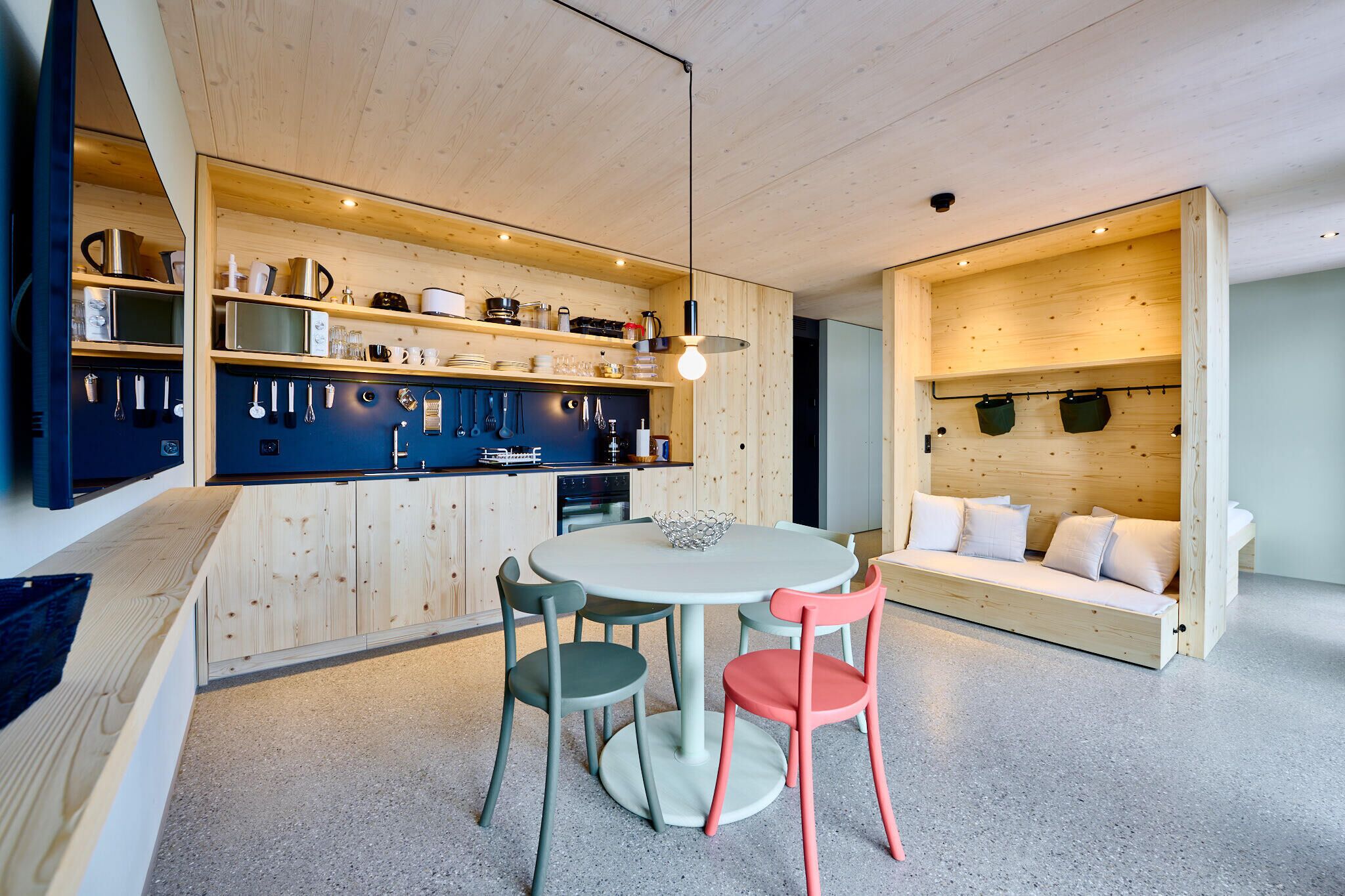 Una cocina moderna con armarios de madera, una mesa redonda para comer y sillas de colores.