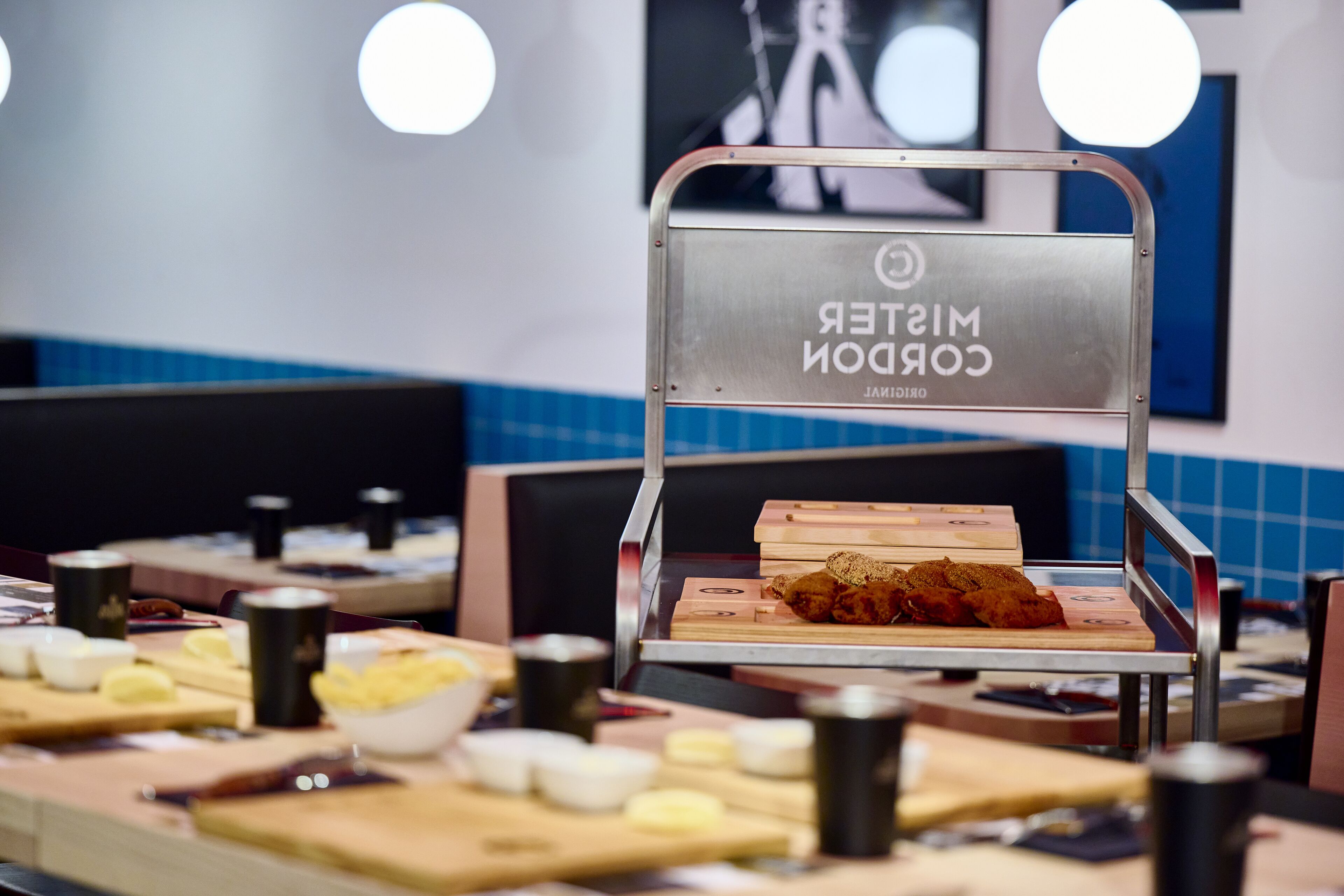 A conveyor belt with a sign reading "Mister CORON" in a dining area with tables and chairs.