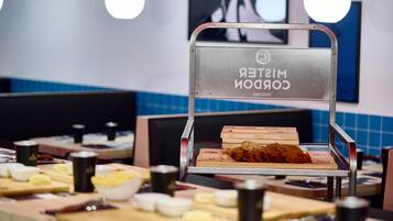 A conveyor belt with a sign reading "Mister CORON" in a dining area with tables and chairs.