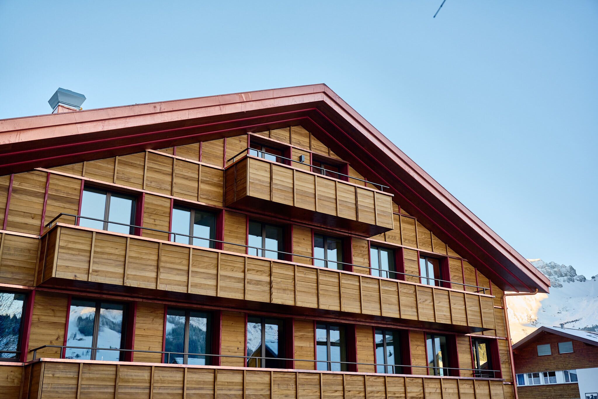 Un edificio de madera de varios pisos con ventanas grandes y techo rojo.