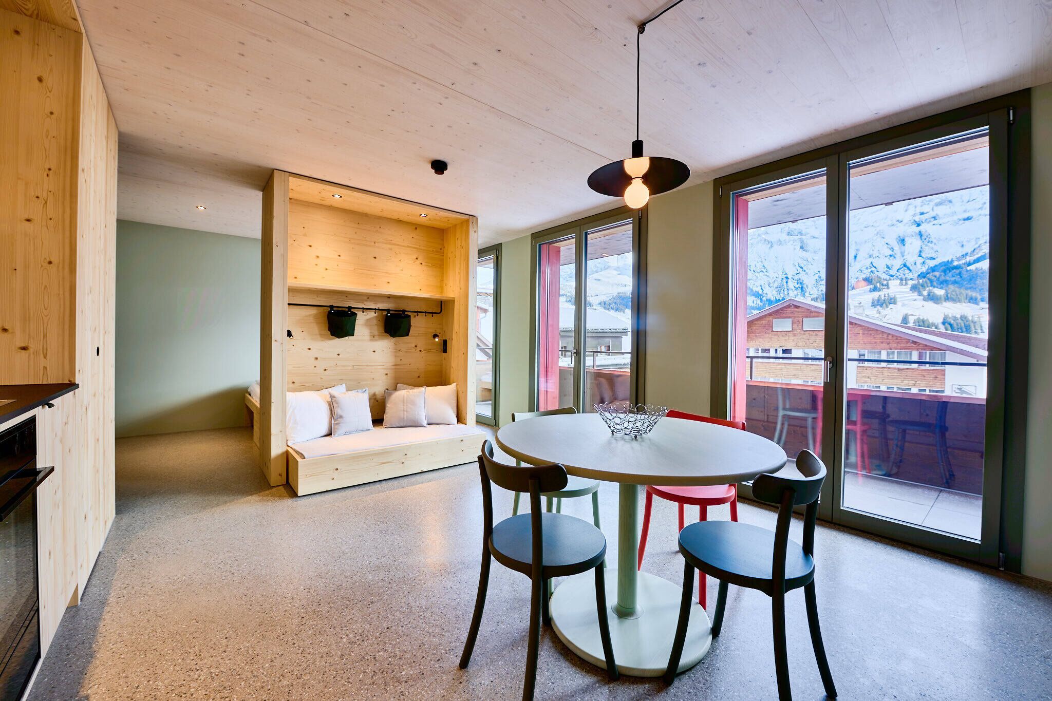 A modern interior with a round table, chairs, a wooden bench, and large windows with a mountain view.