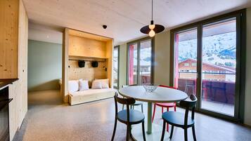 A modern interior with a round table, chairs, a wooden bench, and large windows with a mountain view.