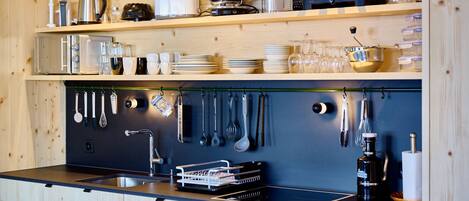 Une cuisine avec des meubles de rangement en bois, un plan de travail noir, ainsi que divers ustensiles et appareils de cuisine.