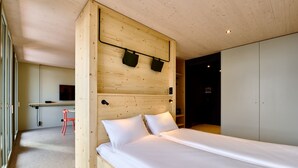Een moderne slaapkamer met een houten hoofdbord, een bed met witte lakens, een bureau met stoel en een garderobe.