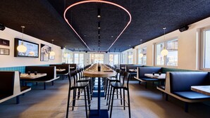 Een modern restaurant met een lange gedeelde tafel, zitjes en hoge plafonds.