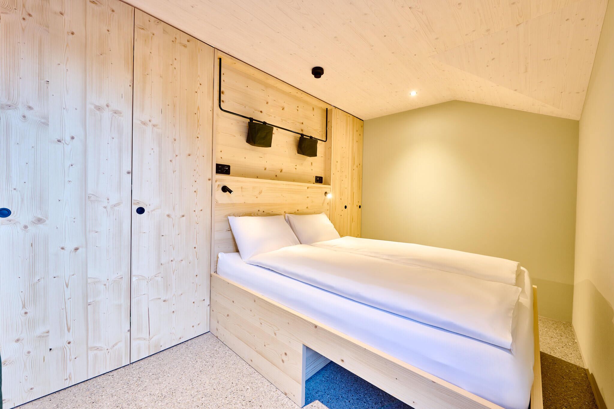 Een slaapkamer met een houten hoofdbord, een bed met wit beddengoed en een klein plankje met twee tassen.
