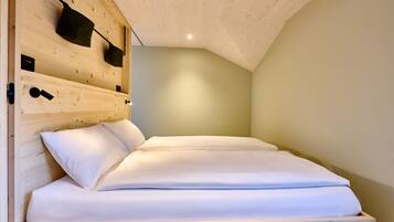 A wooden bunk bed with white bedding, a headboard with storage pockets, and a sloped ceiling.