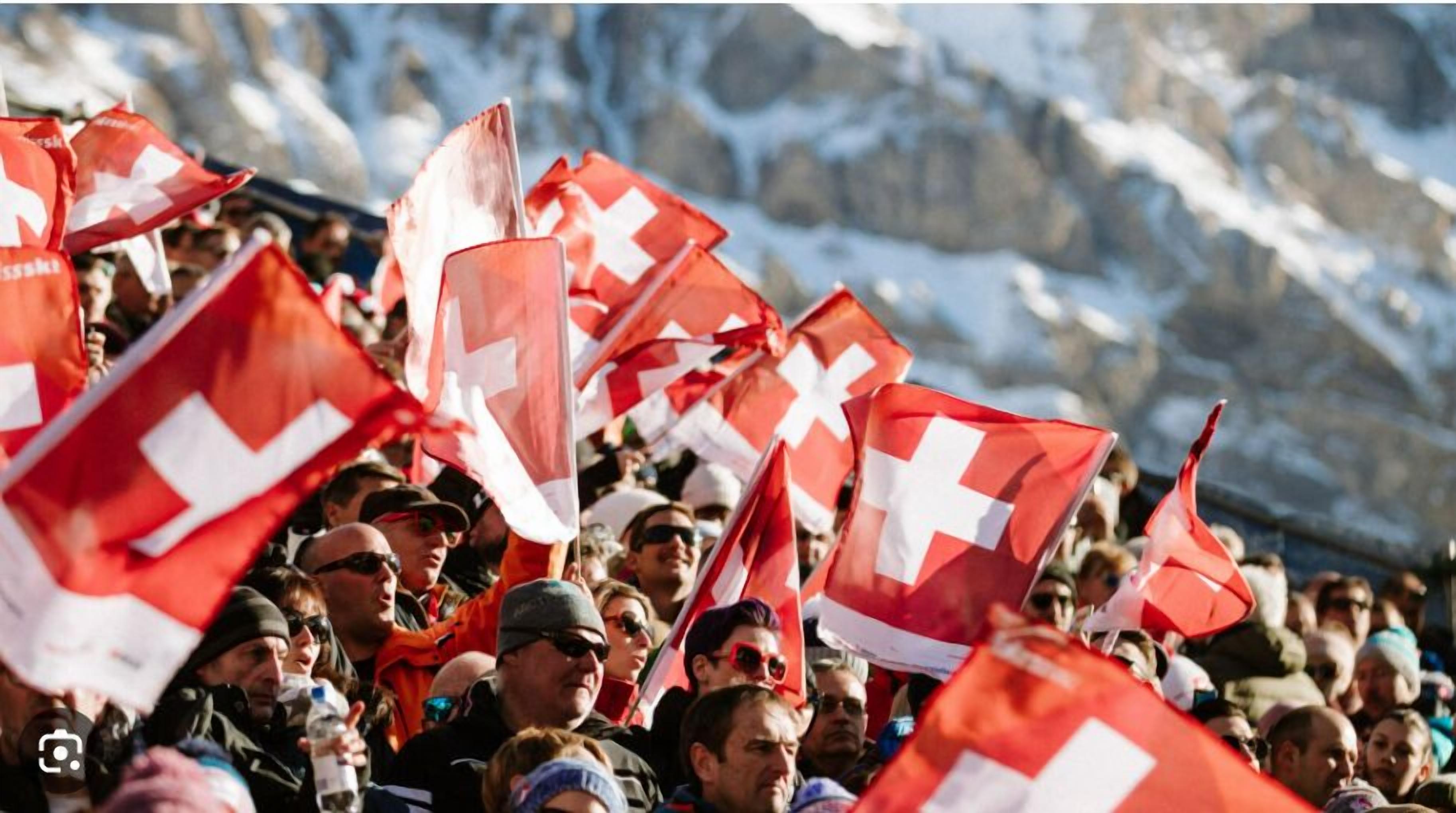 A crowd of people holding red and white flags, likely at a public event or gathering.