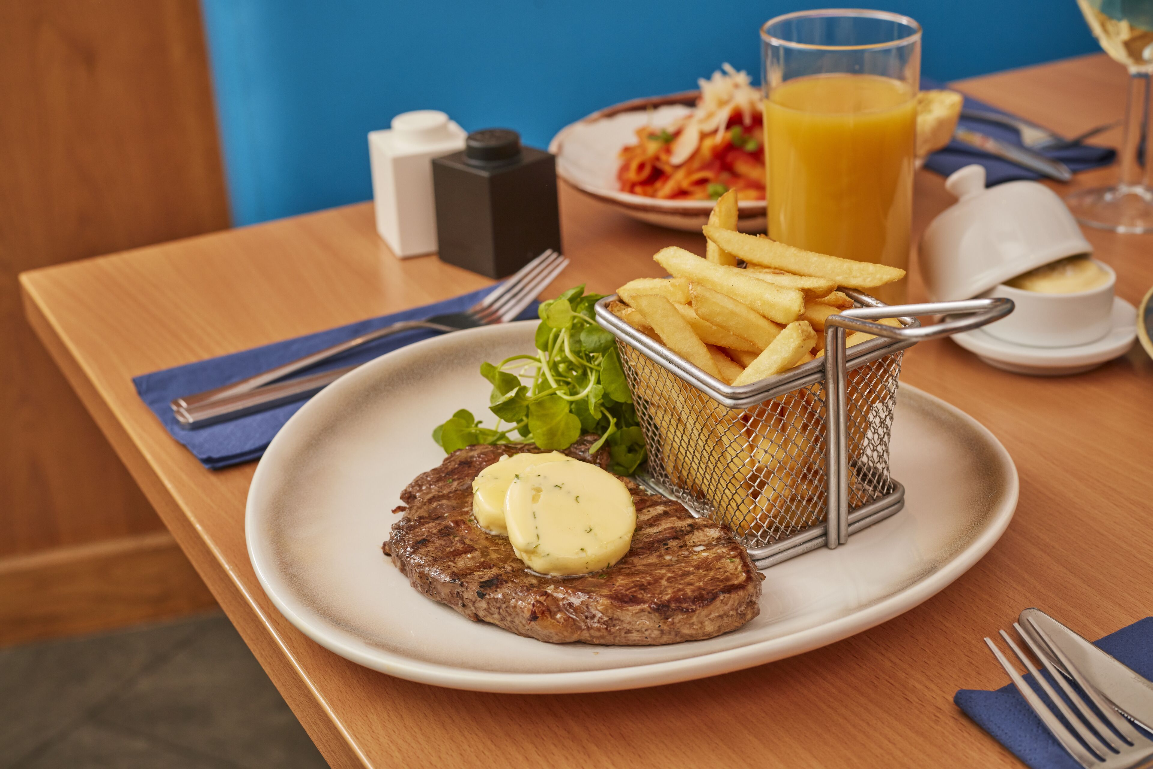 A plate with a steak and fries, a glass of orange juice, and a side salad on a wooden table.