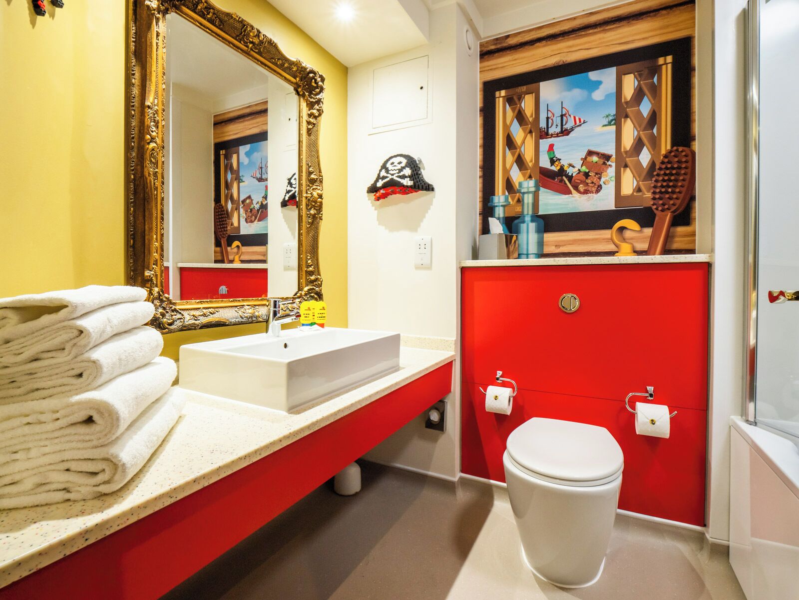 A bathroom with a white sink, a red vanity, a white toilet, and a large mirror with an ornate frame.
