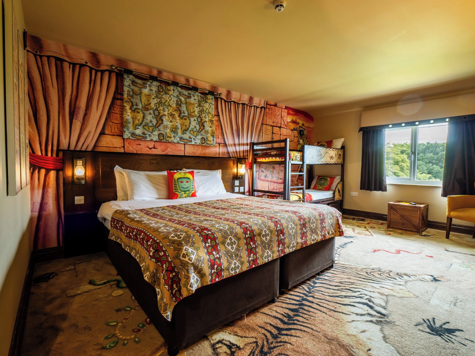 A bedroom with a bunk bed, a patterned bedspread, a headboard with a tapestry, and a window with curtains.