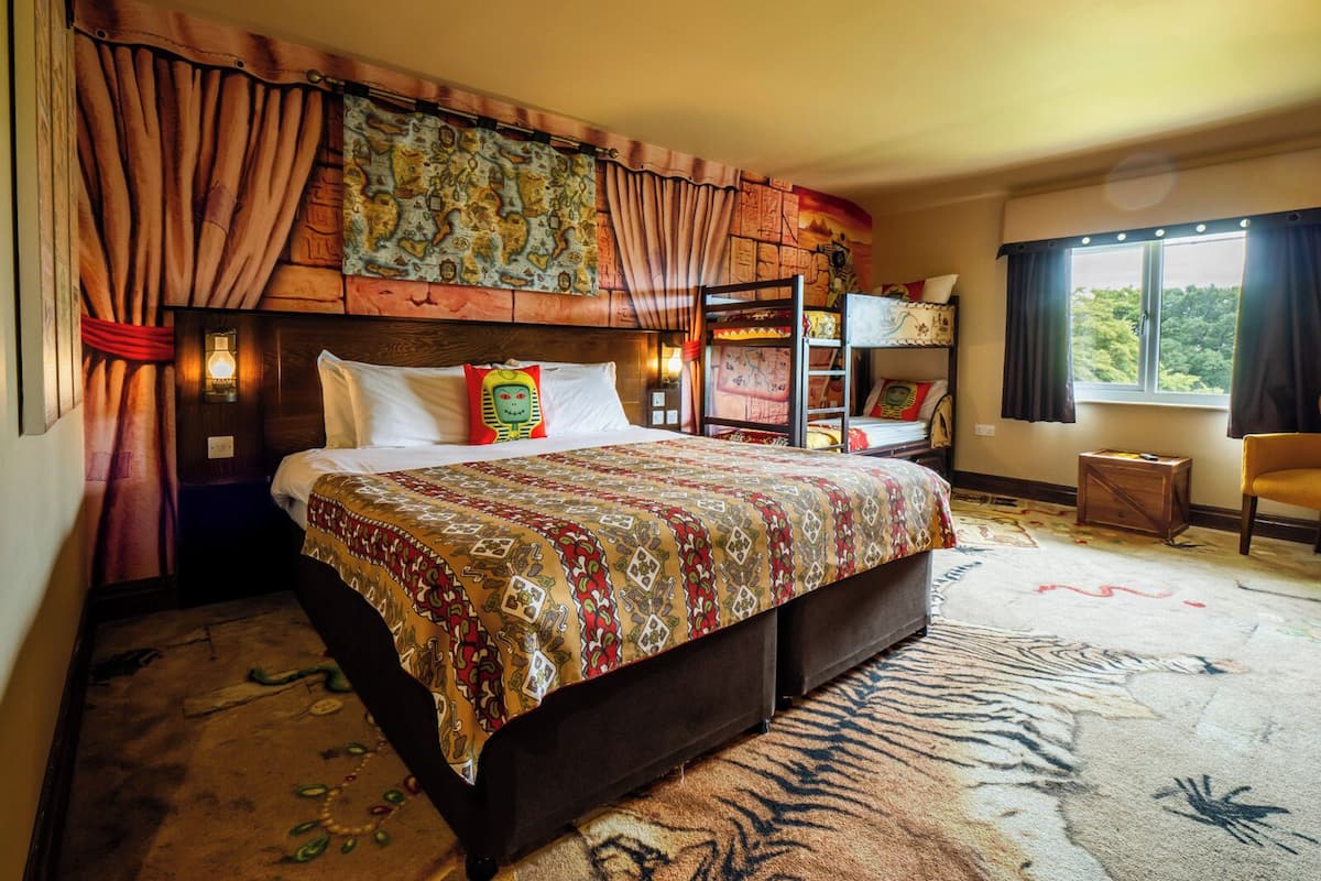 A bedroom with a bunk bed, a patterned bedspread, a headboard with a tapestry, and a window with curtains.