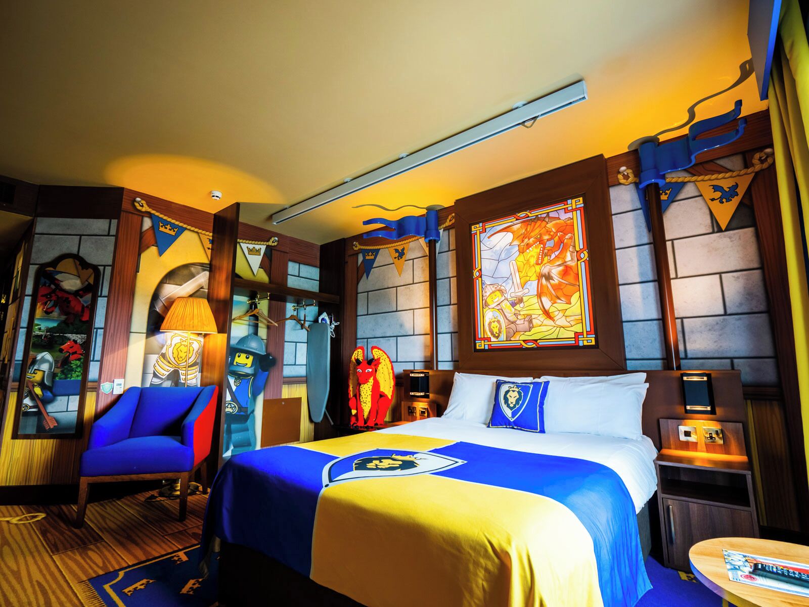 A hotel room with a bed, a chair, a nightstand, and a wall with a stained glass window.