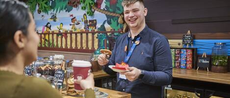 A person serving food at a counter with a wooden backdrop and a mural.