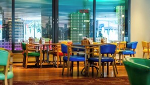 A modern dining area with wooden tables and chairs, large windows with a cityscape view, and a patterned carpet. - LEGOLAND Windsor Resort (Windsor)