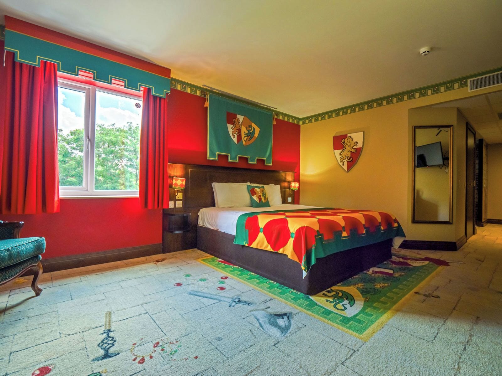 A bedroom with a large bed, red curtains, and a window with a view of trees.
