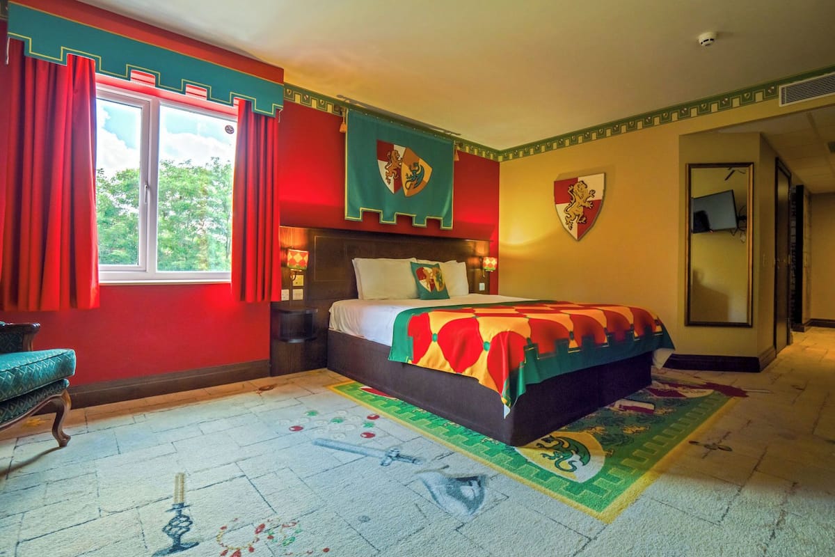 A bedroom with a large bed, red curtains, and a window with a view of trees.