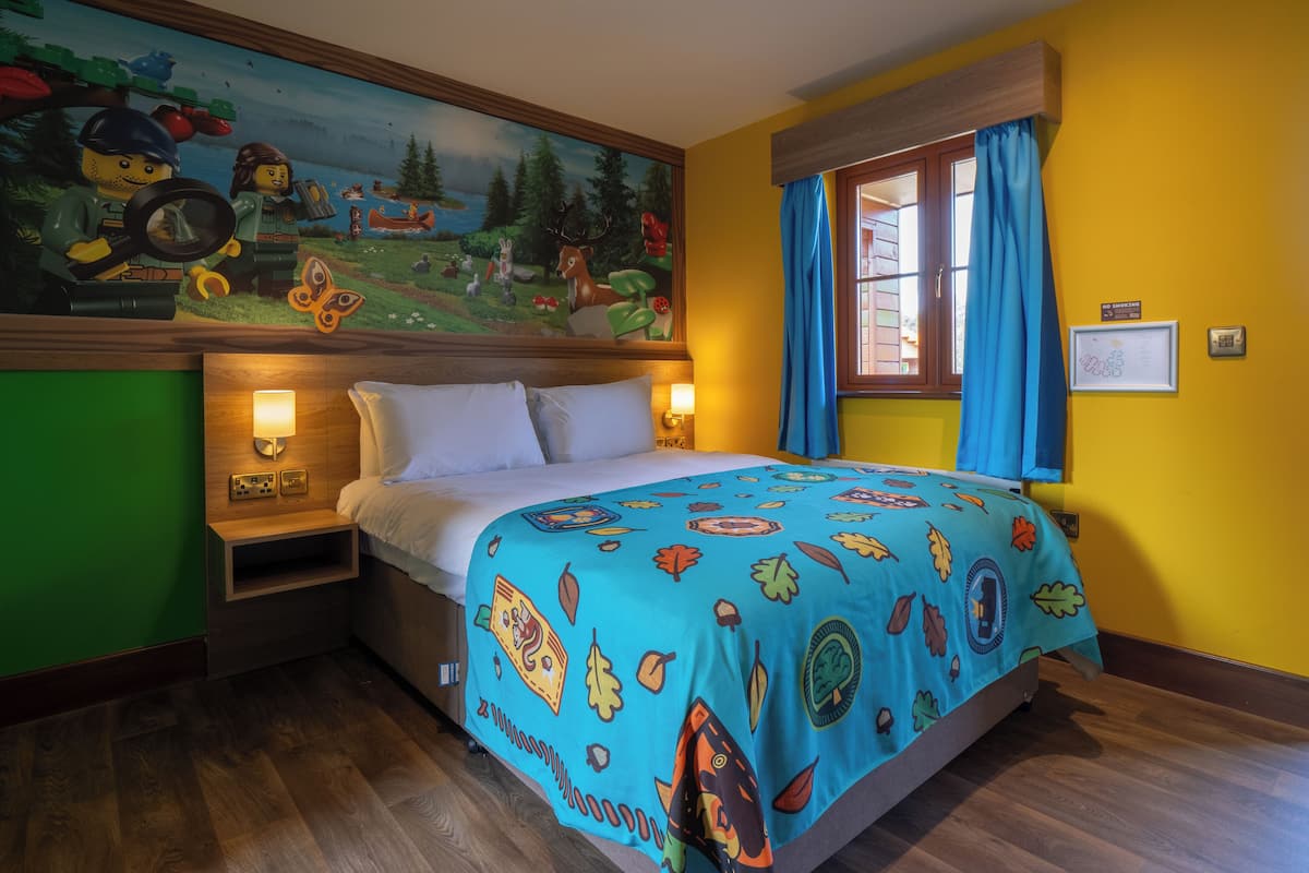 A bedroom with a bed, a nightstand, a wall mural, a window with curtains, and a 'No Smoking' sign.