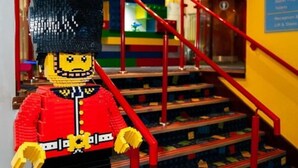 A LEGO figure in a red uniform standing in front of a staircase with red railings. - LEGOLAND Windsor Resort (Windsor)