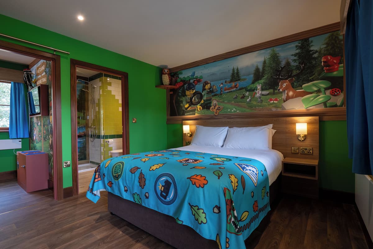 A bedroom with a bed, a mural, a wooden headboard, and a nightstand.