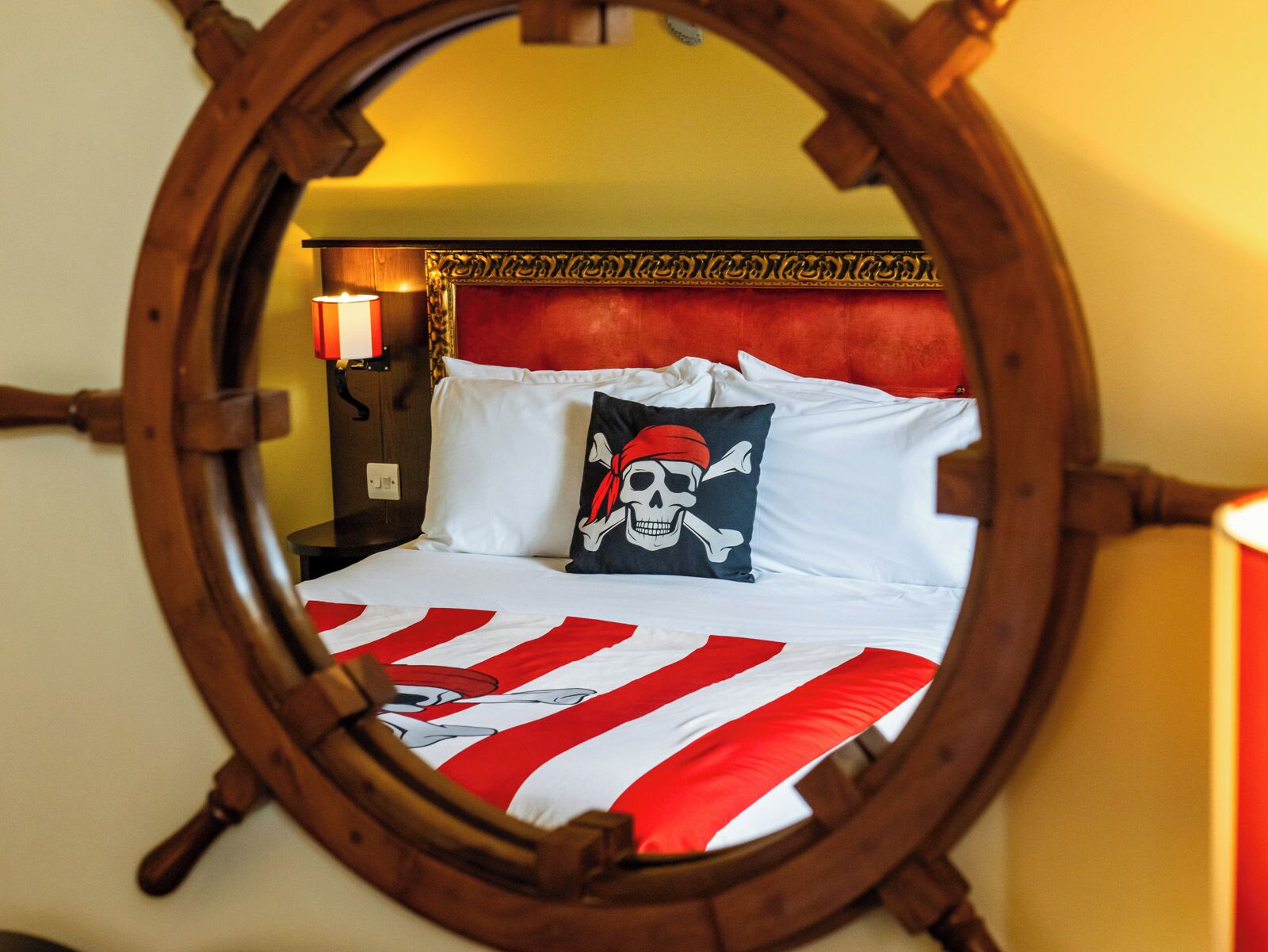 A bed with a red and white striped bedspread, a skull and crossbones pillow, and a wooden headboard.