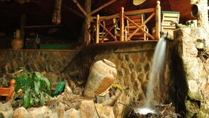 A rustic interior with a stone wall, a wooden bench, a hanging basket, and a small waterfall feature. - Naiberi Resort (Eldoret)