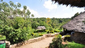 A rustic thatched-roof hut with a stone pathway leading to a lush garden. - Naiberi Resort (Eldoret)