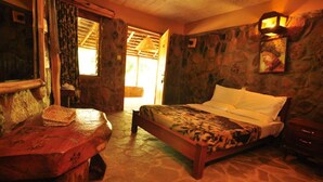 A cozy room with a bed, a wooden table, and a stone wall. - Naiberi Resort (Eldoret)