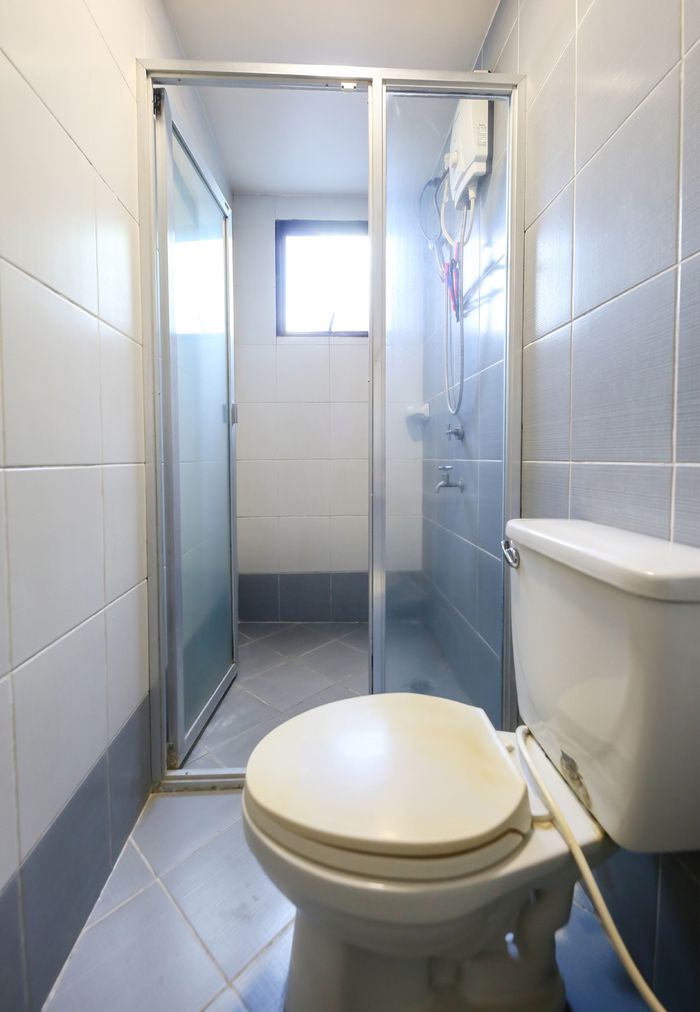 Un baño con inodoro, cabina de ducha y ventana que proporciona luz natural.